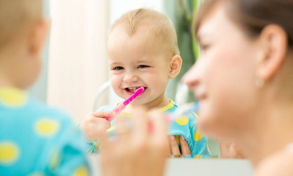 Une mère s'entraîne à se brosser les dents avec son bébé. Le petit enfant a une brosse à dents dans la bouche, ce qui fait que le dentifrice peut facilement être avalé.