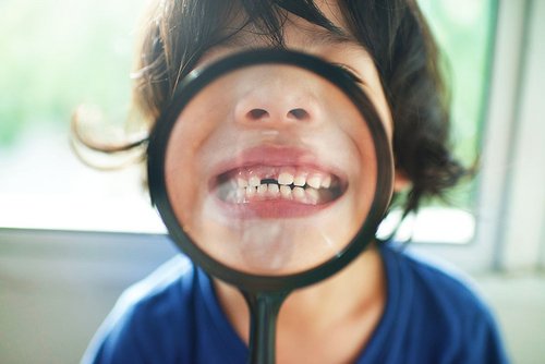 Un enfant montre sa première dent manquante avec une loupe devant la bouche pour symboliser le début du changement de dents chez les enfants.