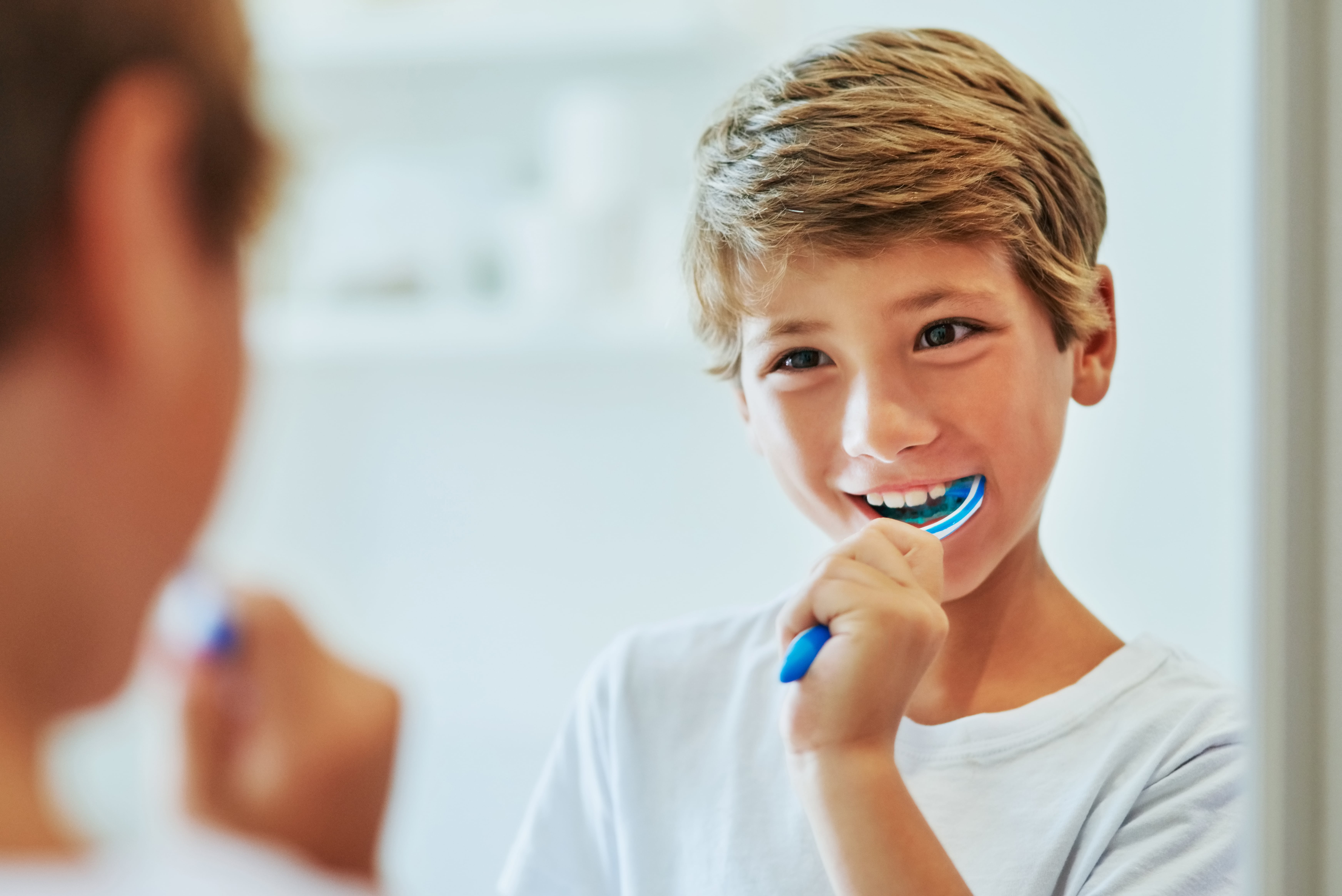 Garçon se tenant devant le miroir avec une brosse à dents dans la bouche comme symbole de la bonne technique de brossage des dents pour les enfants.