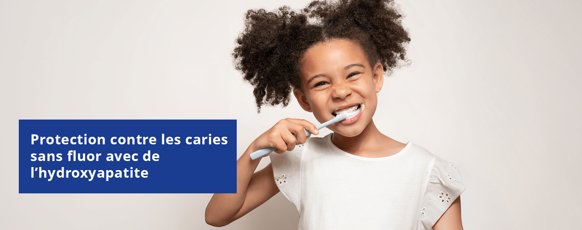 Une jeune fille sourit, montrant ses dents qui ont des taches blanches. Une boîte de texte indique : « Protection contre les caries sans fluor avec de l'hydroxypatite ».